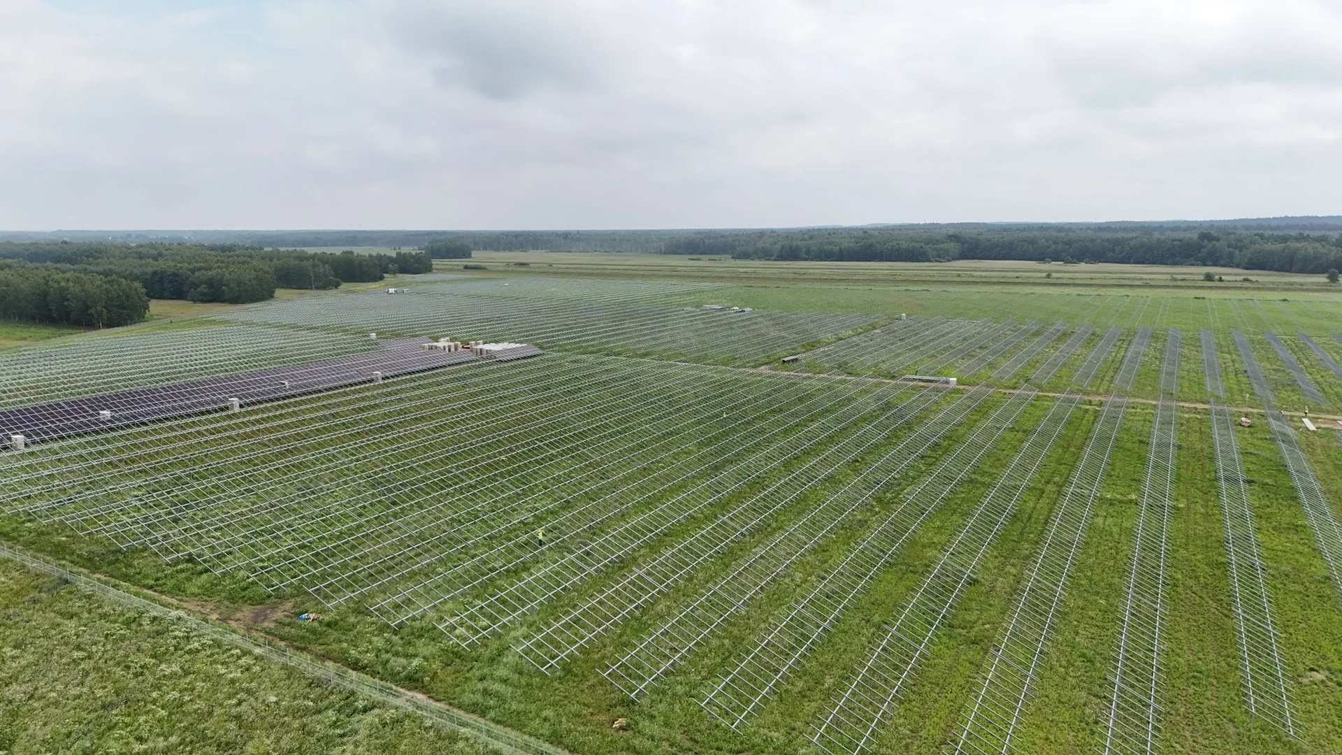 Widok z drona na duże pole ze stalową konstrukcją pod moduły i pierwszym rzędem zamontowanych modułów