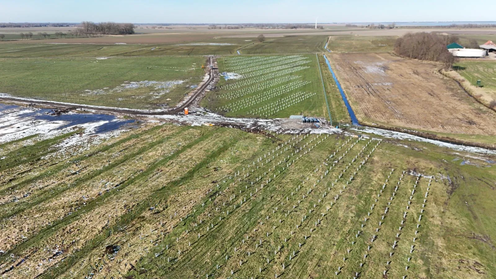 Widok z drona na pole z rzędami jasnych słupków, drogą polną i kanałem z wodą w zimowej scenerii